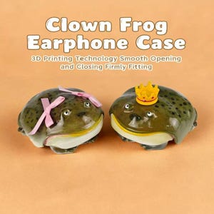 Peut inclure: Deux étuis pour écouteurs originaux en forme de grenouilles. L'une a un nœud rose, l'autre une couronne dorée. Les étuis sont verts avec des taches noires et des ventres blancs. Le texte sur l'image indique "Clown Frog Earphone Case".