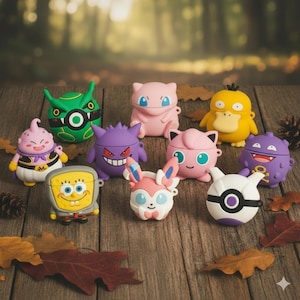 May include: A selection of colourful AirPod cases, each designed to resemble cartoon characters. The cases are in various colours, including yellow, pink, purple, green, and white. They are displayed on a wooden surface with autumnal leaves.