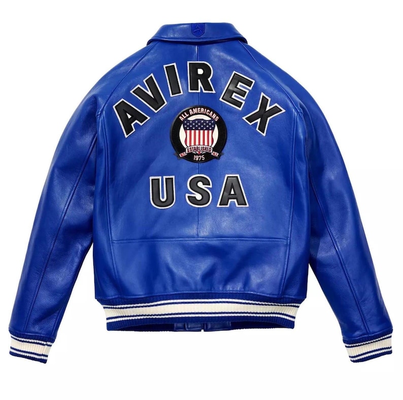 May include: A vibrant blue leather jacket featuring the word "AVIREX" in white across the upper back. Below, the word "USA" is displayed in white. A circular patch with the words "ALL AMERICANS" and "ESTABLISHED 1975" is centered above the "USA" text.