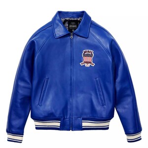 May include: A striking blue leather jacket in a bomber style. It has a collared neckline, a front zip, and a chest patch with the brand name and a patriotic design. The cuffs and hem have white stripes.