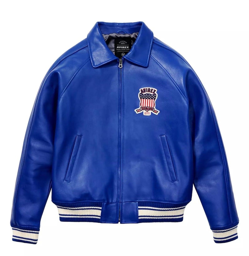 May include: A striking blue leather jacket in a bomber style. It has a collared neckline, a front zip, and a chest patch with the brand name and a patriotic design. The cuffs and hem have white stripes.