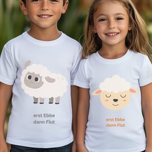 Könnte beinhalten: Zwei weiße T-Shirts mit kurzen Ärmeln und Schaf-Grafiken. Das linke T-Shirt zeigt ein ganzes Schaf mit dem Text "erst Ebbe dann Flut". Das rechte T-Shirt zeigt einen Schafkopf mit geschlossenen Augen und dem Text "erst Ebbe dann Flut" in Orange.
