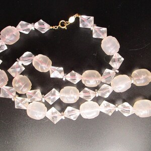 May include: A vintage necklace featuring alternating clear, faceted, diamond-shaped beads and frosted, oval-shaped beads. The necklace has a gold-colored clasp and is displayed against a black background. The beads are strung together with a delicate, nearly invisible thread.