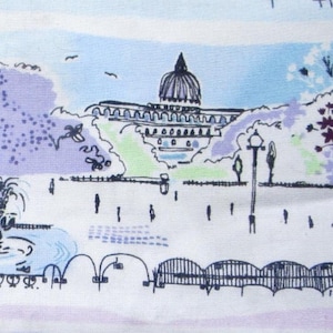 May include: A fabric print featuring a park scene with a domed building, fountain, and trees. The illustration uses shades of blue, purple, and green, with black outlines. The design includes a fountain, people, and a bridge.