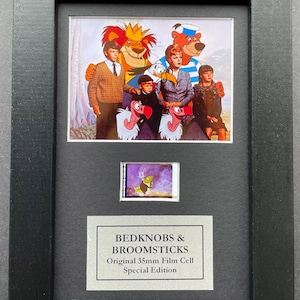 May include: A framed film cell from "Bedknobs & Broomsticks." The frame contains a larger image of characters from the film, including a lion, bear, and children. Below is a smaller film cell and a plaque with the film's title.
