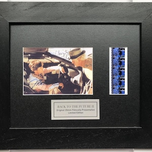 May include: A white ceramic mug with a black handle and the text "But First, Coffee" in a bold, black font. The mug is set against a blurred background. The mug appears to be approximately 10 cm tall.