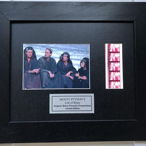 May include: Black framed print of a scene from Monty Python's Life of Brian, including a film strip and a plaque. The frame surrounds a photo of the film's cast and a strip of film cells. The plaque reads "Monty Python's Life of Brian", a limited edition.