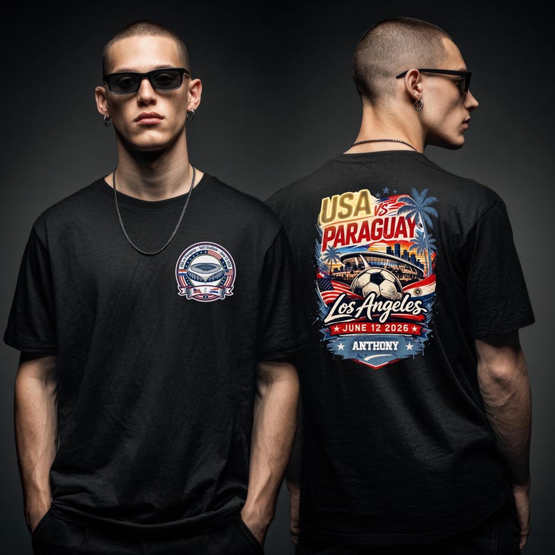 Front and back view of a black t-shirt worn by a model, featuring a small chest emblem on the front and a large vibrant graphic on the back reading “USA vs Paraguay, Los Angeles, June 12 2026, Anthony.” The back design includes a stadium, soccer ball, palm trees, skyline, and American flag elements. Stylish lifestyle mockup showcasing a bold soccer fan shirt perfect for match day and sports events.