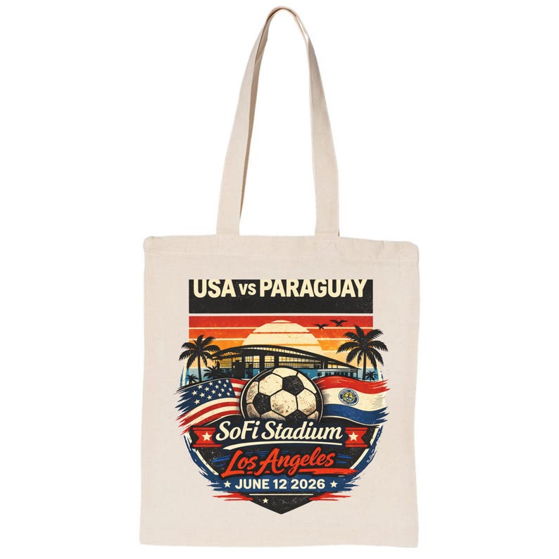 May include: Cream-colored tote bag featuring a soccer ball and the text "USA vs Paraguay" above a stadium graphic. The design includes the flags of the USA and Paraguay, palm trees, and the text "SoFi Stadium Los Angeles June 12 2026."