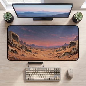 May include: A rectangular desk mat featuring a printed landscape of a desert filled with abandoned, sand-covered computer monitors under a sunset sky. The mat has a black border and is positioned on a light wood surface with a keyboard and mouse.