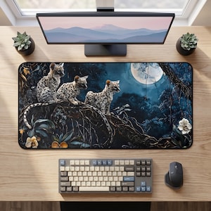 May include: A rectangular desk mat featuring a dark, nocturnal forest scene with three spotted ocelot kittens perched on a thick tree branch under a large, glowing full moon. The artwork includes deep blue shadows, tangled roots, and white flowers.