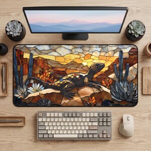 Könnte beinhalten: Eine rechteckige Schreibtischunterlage mit einer Illustration im Buntglas-Stil, die eine Eidechse in einer Wüstenlandschaft mit Kakteen und Sukkulenten zeigt. Das Design verwendet warme Bernstein-, Braun- und Blautöne. Die Unterlage liegt auf einem Holztisch mit einem Computermonitor, einer mechanischen Tastatur und einer Computermaus.