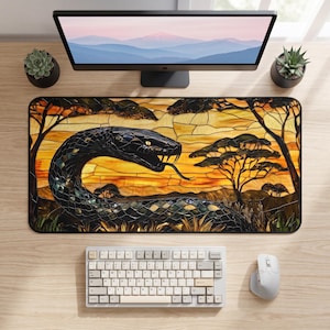 May include: A rectangular desk mat featuring a stained glass style illustration of a black snake with its tongue out, set against a golden sunset landscape with silhouetted acacia trees. The design uses dark and warm yellow tones throughout.