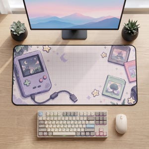 May include: A rectangular desk mat featuring a light purple handheld gaming console, three game cartridges, and yellow star icons on a grid background. The console screen displays a pixel art landscape with a cat, moon, and stars in a night sky.