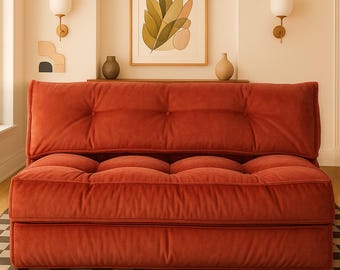 Puede incluir: Un sofá bajo de terciopelo color óxido con respaldo y cojín de asiento capitoné. El sofá presenta una silueta rectangular y cuadrada con un acolchado grueso y mullido, además de una textura de tela suave y mate en su superficie.