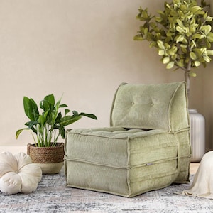 May include: A light green corduroy armchair with a tufted back and seat. The chair has a low profile and a relaxed design. The image also shows a potted plant, a decorative pillow, and a rug.