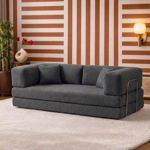 Puede incluir: Un sofá moderno gris con tres cojines de respaldo y dos reposabrazos. El sofá tiene un perfil bajo y un marco de metal en el lateral. El sofá está sobre una alfombra blanca, y el fondo tiene un patrón de rayas en marrón y blanco.