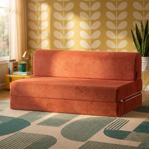 May include: A rust-colored velvet sofa bed with a rectangular backrest and a thick seat cushion. The piece features a low-profile design with a smooth, solid-colored fabric finish and a foldable structure that allows it to transition into a flat surface.