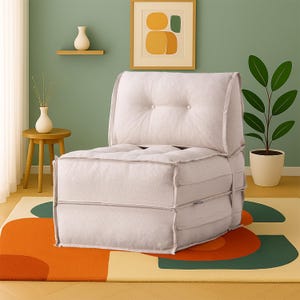 Puede incluir: Un sillón modular beige claro, con mechones, con respaldo abotonado. La silla está colocada sobre una alfombra colorida con formas geométricas naranjas, verdes y amarillas. Una pequeña mesa auxiliar de madera y una planta en maceta también están en la escena.