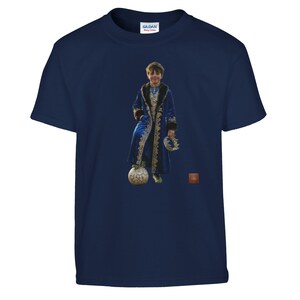 以下が含まれることがあります： ネイビーブルーのギルダンTシャツ。金色のトリムが付いた青いローブを着た人物が、王冠を持ち、サッカーボールの上に立っているフルカラーの画像が特徴です。その人は微笑んでいます。背景は草地です。