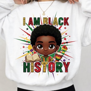 Op de afbeelding: Witte sweatshirt met de tekst "I AM BLACK HISTORY" in kleurrijke letters. De afbeelding toont een cartoonillustratie van een zwart kind met een boek, een trommel en een vuist, omringd door kleurrijke sterren.