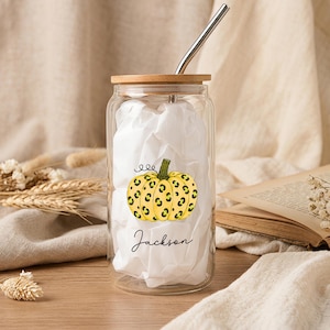 May include: A clear glass tumbler with a bamboo lid and a metal straw. The glass features a yellow pumpkin graphic with a black leopard print pattern and the name Jackson printed in black script lettering below the pumpkin illustration.