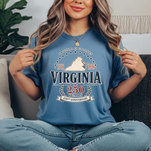 May include: A blue t-shirt with the text "Virginia 250 Years 250th Anniversary" and a map of Virginia. The shirt also has the text "Original 13 Colonies 1776-2026".