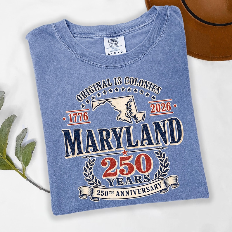 May include: A light blue t-shirt with the text "ORIGINAL 13 COLONIES" and "MARYLAND 250 YEARS 250TH ANNIVERSARY". The shirt has a crew neck and short sleeves. The shirt is a size L-G-G.