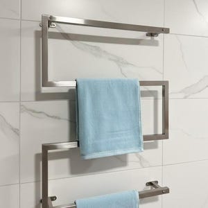 May include: A modern, stainless steel towel warmer mounted on a white tiled wall. The geometric design features three horizontal bars for hanging towels. Two light blue towels are neatly displayed on the warmer, adding a pop of color to the bathroom.