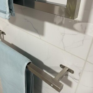 May include: A modern bathroom scene featuring a light blue towel hanging on a brushed nickel towel bar. The towel bar is mounted on a white marble tile wall. Another towel bar is visible in the background.