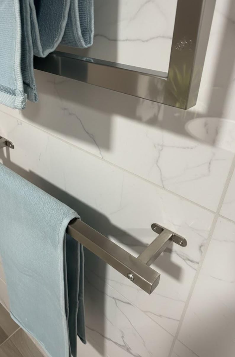 May include: A modern bathroom scene featuring a light blue towel hanging on a brushed nickel towel bar. The towel bar is mounted on a white marble tile wall. Another towel bar is visible in the background.