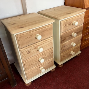 May include: Two matching bedside chests, each featuring four drawers with natural wood grain fronts and cream-coloured frames. The tops are finished in a light natural wood tone, and each drawer is fitted with a round, cream-coloured wooden knob.