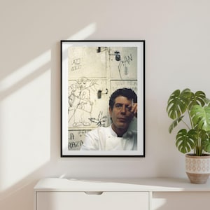 May include: A framed photographic print featuring a person in a white chef coat standing before a wall covered in black ink graffiti. The person holds a cigarette near their face. The wall displays various sketches and the text LA RAZA.