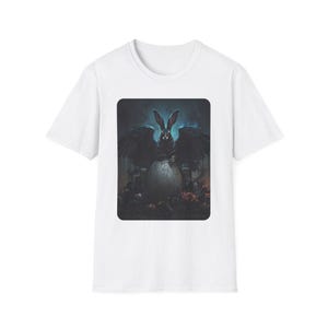 Puede incluir: Camiseta blanca con una ilustración gótica oscura de un conejo alado emergiendo de un huevo agrietado. La obra de arte está detallada con tonos de negro, azul y rojo, creando un diseño dramático y de fantasía.