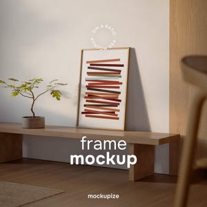 May include: A framed art print with a gold frame featuring a design of horizontal lines in shades of red, brown, and green. The words "frame mockup" are displayed in white text. A small potted plant sits on a wooden shelf.