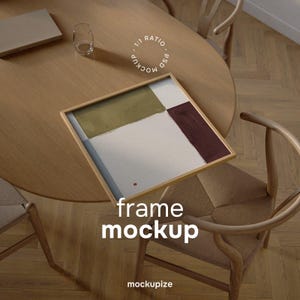 May include: A square framed artwork with abstract color blocks in olive green, burgundy, and white, resting on a light wood table. The text "frame mockup" is displayed in white. A glass and a laptop are also on the table.