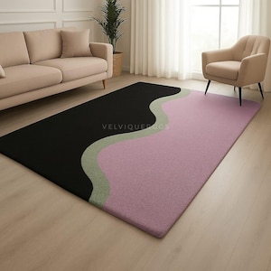 May include: A rectangular area rug with a modern design. The rug features a black section on the left, a wavy light green stripe, and a pink section on the right. The rug is on a hardwood floor.