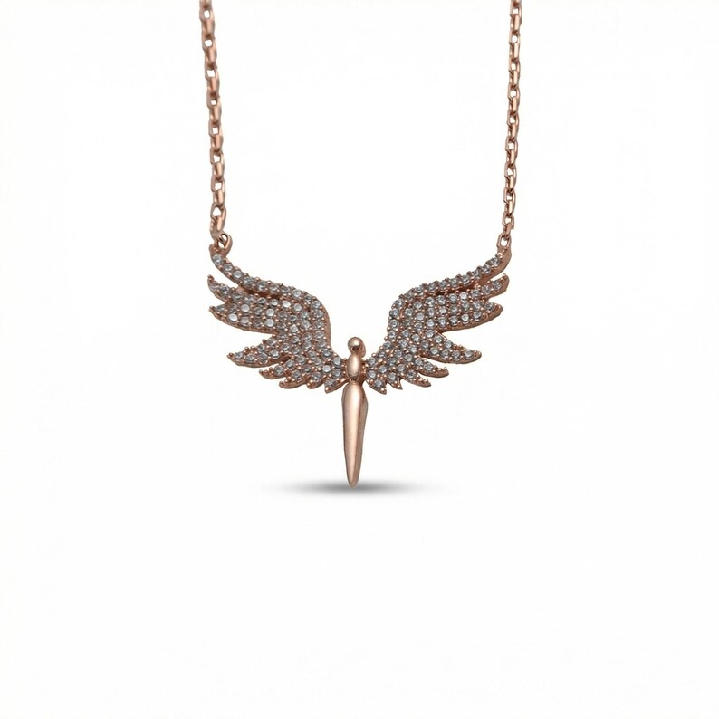 May include: Rose gold-toned necklace featuring an angel pendant. The pendant has outstretched wings encrusted with small, clear gemstones. The angel's body is a vertical, pointed shape. The chain is a delicate link style.