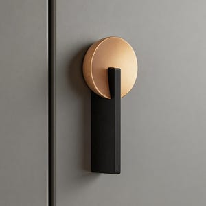 May include: A cabinet pull featuring a circular, brushed brass handle and a rectangular, black base. The hardware is mounted on a grey cabinet door, showcasing a modern design.