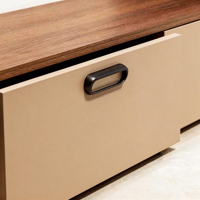 Pu&ograve; includere: Primo piano di un cassetto di un mobile moderno, marrone chiaro, con una maniglia scura a forma ovale. Il cassetto &egrave; parzialmente aperto, rivelando un piano in legno scuro. Il mobile ha un design minimalista.