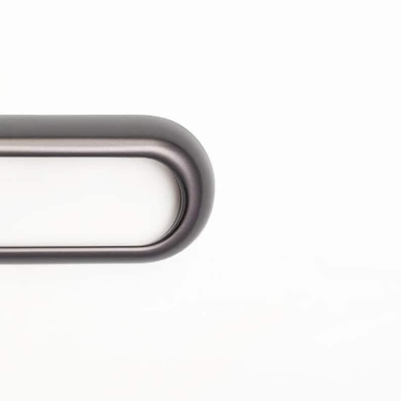 Pu&ograve; includere: Primo piano di una maniglia per mobili ovale grigio scuro con interno bianco. La maniglia ha un design liscio e arrotondato ed &egrave; posta su uno sfondo bianco. Questo hardware &egrave; adatto per cassetti e armadi.