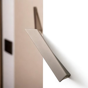 Op de afbeelding: Een moderne, schuine deurklink in een geborstelde zilveren afwerking. De klink is gemonteerd op een witte deur, met een neutraal getinte muur zichtbaar op de achtergrond. Het ontwerp is minimalistisch en strak.