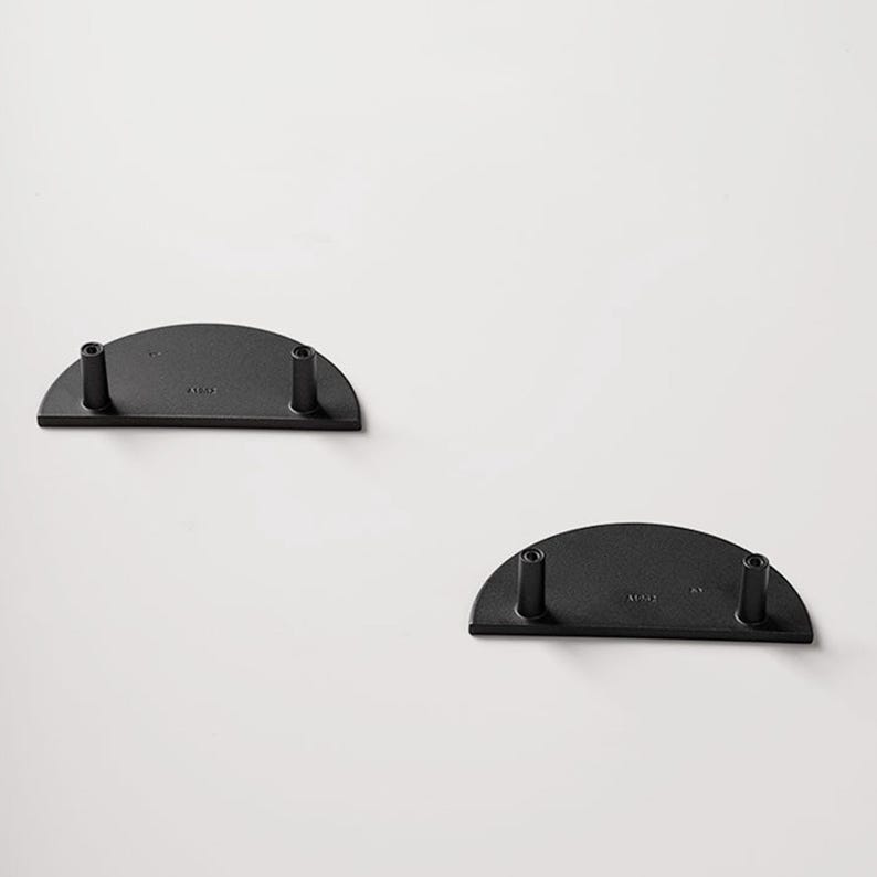 Op de afbeelding: Twee zwarte, halfronde metalen plankbeugels met elk twee cilindrische palen. De beugels zijn op een witte achtergrond geplaatst. De beugels zijn waarschijnlijk bedoeld om planken of andere decoratieve items te ondersteunen.