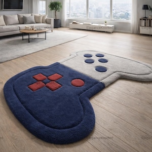 May include: A large, plush rug shaped like a video game controller. The rug is primarily navy blue and gray, with red and blue button details. The rug is on a hardwood floor.