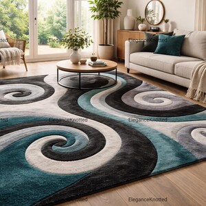 May include: A rectangular rug featuring a flowing, abstract design in teal, grey, white, and black. The rug is laid on a wooden floor in a living room. The pattern creates a sense of movement and adds a contemporary feel to the room's decor.