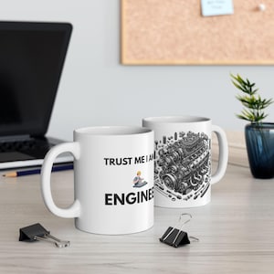 Può includere: Due tazze di ceramica bianca. Una tazza ha il testo "TRUST ME I AM ENGINEER" con un ingegnere dei cartoni animati. L'altra tazza ha un'illustrazione dettagliata in bianco e nero di un motore. Entrambe le tazze hanno un manico bianco.