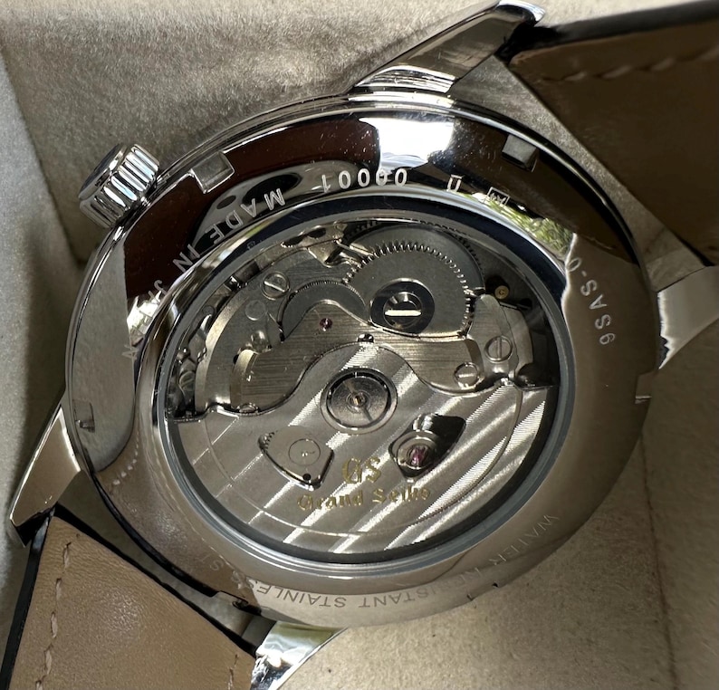 May include: A stainless steel wristwatch with an exhibition case back revealing the internal mechanical movement. The rotor is engraved with the Grand Seiko logo. Text on the case back includes 9SAS-0, MADE IN JAPAN, and WATER RESISTANT STAINLESS STEEL.