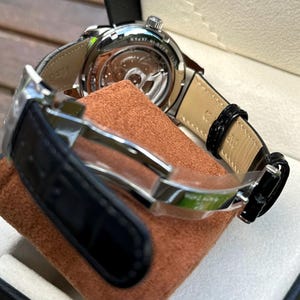 May include: A stainless steel wristwatch with a black leather strap and a deployment clasp. The watch features an exhibition case back revealing the internal movement, with the text MADE IN JAPAN and STAINLESS STEEL engraved on the metal casing.