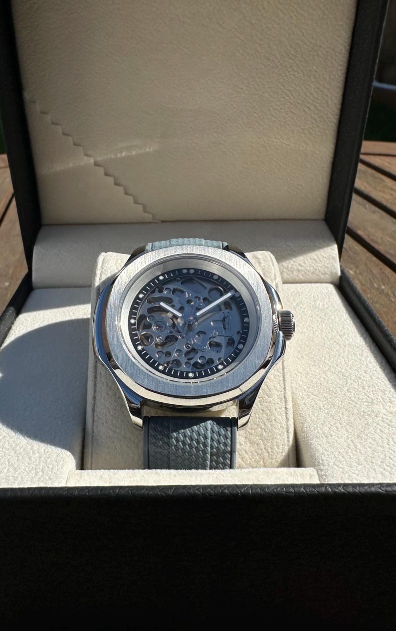 Peut inclure: Une montre squelette argent&eacute;e avec un bracelet en cuir bleu, pr&eacute;sent&eacute;e dans un coffret noir avec un int&eacute;rieur cr&egrave;me. Le cadran r&eacute;v&egrave;le le m&eacute;canisme interne de la montre.