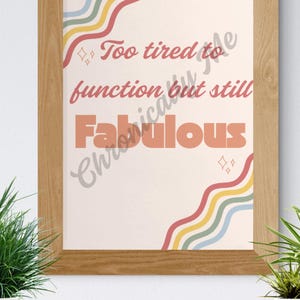 May include: A framed print with a light beige background and the text "Too tired to function but still Fabulous" in a retro font. The design includes colourful wavy lines in red, yellow, green, and blue. The frame is made of light brown wood.